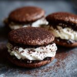 A close-up of a decadent tiramisu cookie sandwich filled with white cream and dusted heavily with cocoa powder.