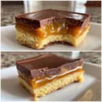 Close-up of a layered twix cookies bar showing a shortbread base, thick caramel layer, and chocolate topping, with a bite taken out.
