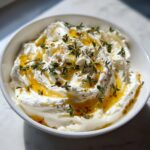 A white bowl filled with fluffy whipped goat cheese, drizzled with golden honey and fresh thyme.