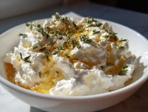 A bowl of fluffy whipped goat cheese drizzled with honey and topped with fresh thyme sprigs.