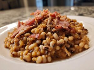 Close-up of a hearty serving of Amazing 1-Pot black eyed peas topped with shredded ham on a white plate.