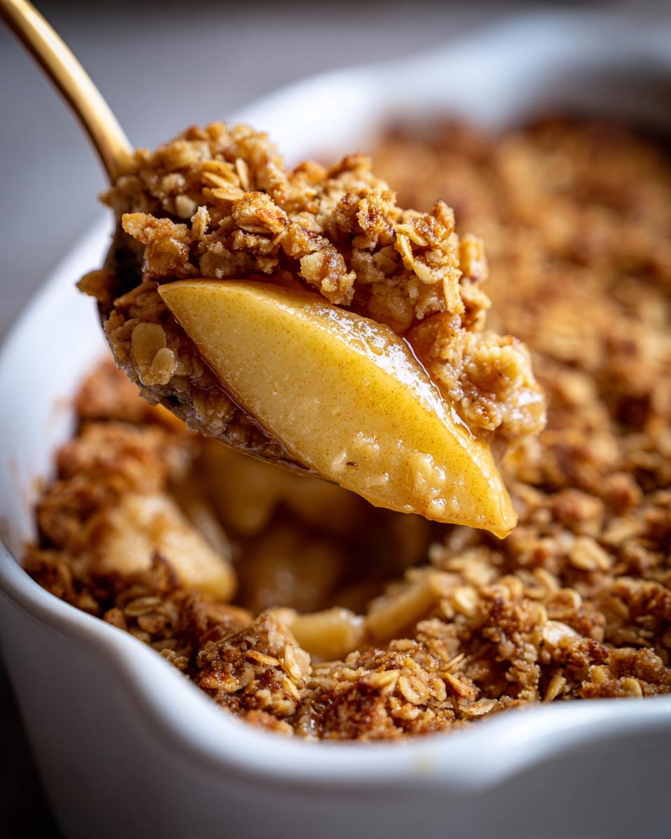 A spoonful of warm apple crumble showing a soft, caramelized apple slice topped with crunchy oat topping.
