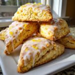 A stack of freshly baked lemon scones topped with white glaze and bright yellow lemon zest.