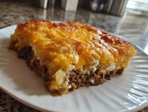 A close-up slice of amazing tater tot casserole featuring a ground meat layer topped with creamy potatoes and melted cheddar cheese.