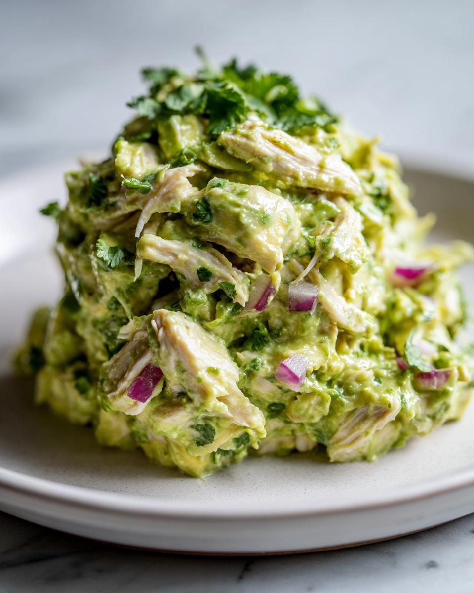 A mound of creamy avocado chicken salad mixed with red onion and topped with fresh cilantro.