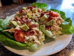 Two servings of creamy blt chicken salad served in crisp lettuce cups, topped with bacon, avocado, and tomato.
