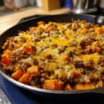 Close-up of a savory sweet potato skillet topped with seasoned ground beef and melted cheddar cheese.