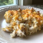 A close-up of a serving of chicken cauliflower rice casserole topped with melted, browned cheddar cheese.