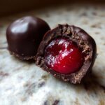 Close-up of a homemade chocolate covered cherries, one whole and one cut in half revealing the bright red, juicy cherry center.