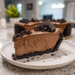 A thick slice of decadent chocolate mousse pie with a dark Oreo crust, topped with cookie crumbles.