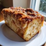 A close-up of a thick slice of baked french toast with a rich, gooey cinnamon streusel topping, served on a white plate.
