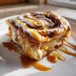 A decadent slice of cinnamon roll apple pie topped with white icing and drizzled generously with caramel sauce.