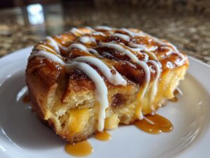 Close-up of a single serving of cinnamon roll apple pie topped with caramel and white icing.