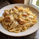 A close-up of creamy chicken alfredo pasta tossed with fettuccine and topped with herbs.