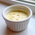 Close-up of creamy garlic sauce with visible minced garlic pieces in a small white ramekin.
