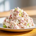 A generous scoop of creamy ham salad recipe with visible chunks of ham and celery on a white plate.