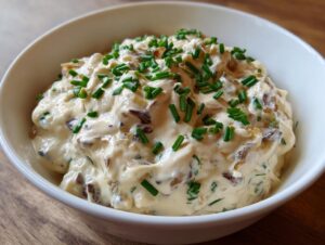 Close-up of a rich, creamy onion dip loaded with caramelized onions and topped generously with fresh green chives.
