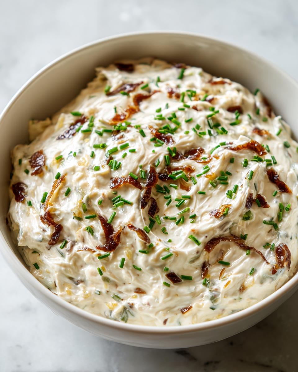 Close-up of a creamy, thick homemade onion dip garnished with crispy fried onions and fresh green chives.