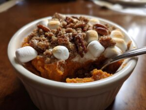 Close-up of a single serving of crockpot sweet potato casserole topped with pecans, streusel, and toasted marshmallows.