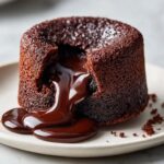 Close-up of a warm chocolate lava cake with the molten center oozing out onto a white plate.