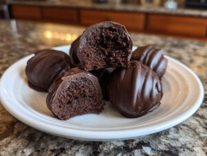 A close-up of several rich chocolate-covered Oreo balls, one cut in half showing the dark, dense interior.