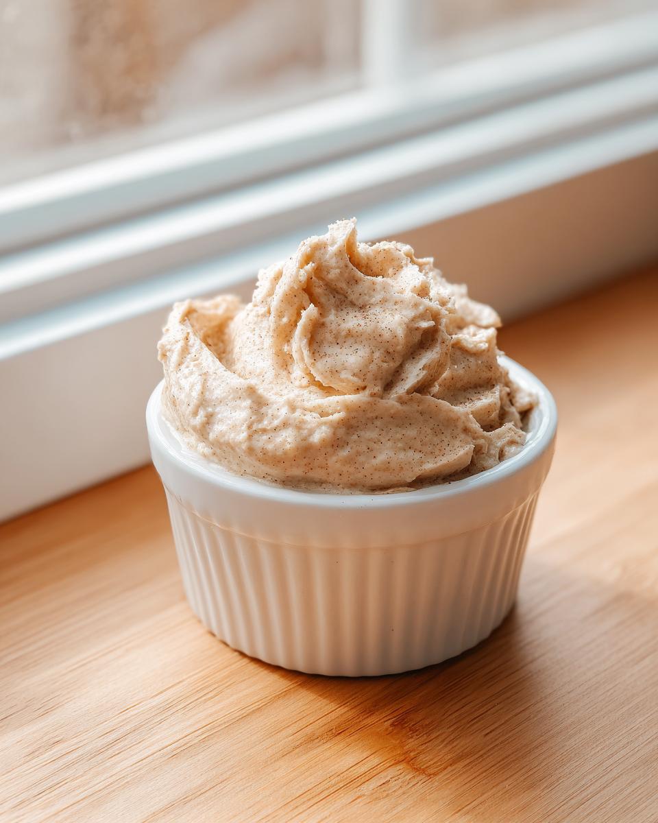 A close-up of fluffy, spiced honey butter recipe mixture swirled high in a small white ramekin on a wooden surface.