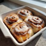 Four freshly baked small batch cinnamon rolls topped with white icing, sitting in a white square baking dish.