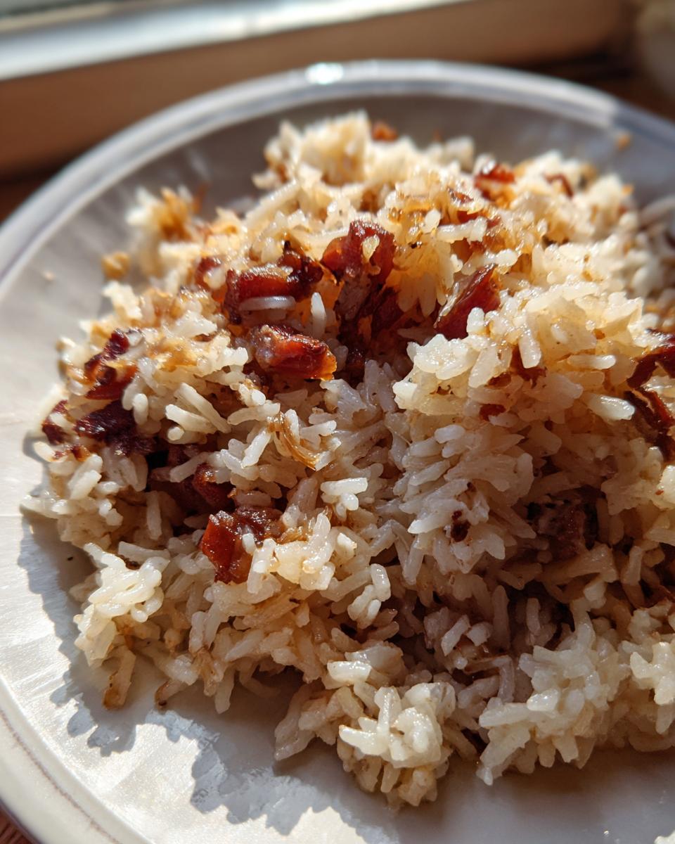 Close-up of a serving of fluffy french onion butter rice topped with dark, caramelized onions on a light plate.