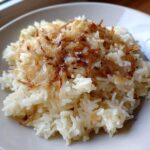 A close-up of fluffy white rice topped generously with caramelized, crispy french onion butter rice topping.