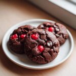 Three fudgy chocolate cherry cookies loaded with dark chocolate chunks and bright red cherries on a white plate.