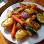 A close-up of vibrant Garlic Herb Roasted Veggies including potatoes, carrots, zucchini, and red onion on a white plate.