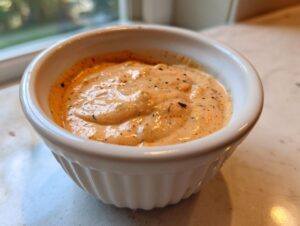 A close-up of creamy, orange-tinted big mac sauce speckled with spices, served in a small white ramekin.