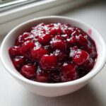 Close-up of thick, glossy cherry pie filling with whole cherries in a white bowl.