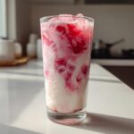 A tall glass filled with iced strawberry milk showing beautiful pink and white swirls over ice cubes.