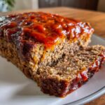 Close-up of a slice of juicy meatloaf topped with a thick, glossy ketchup glaze.