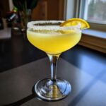 A vibrant yellow lemon drop martini in a coupe glass with a thick sugar rim and lemon slice garnish.