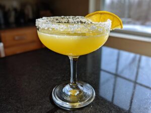 A bright yellow lemon drop martini in a coupe glass with a thick sugar rim and lemon wheel garnish.