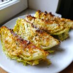 Three roasted cabbage wedges topped with melted cheese and herbs, ready to eat from a white plate.