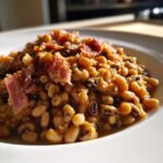 Close-up of a white bowl filled with savory black eyed peas stewed with pieces of smoked ham.