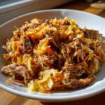 Close-up of shredded pork and sauerkraut mixture with visible shredded carrots in a white bowl.