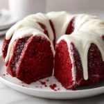 A slice cut from a vibrant red velvet bundt cake topped with dripping white cream cheese glaze.