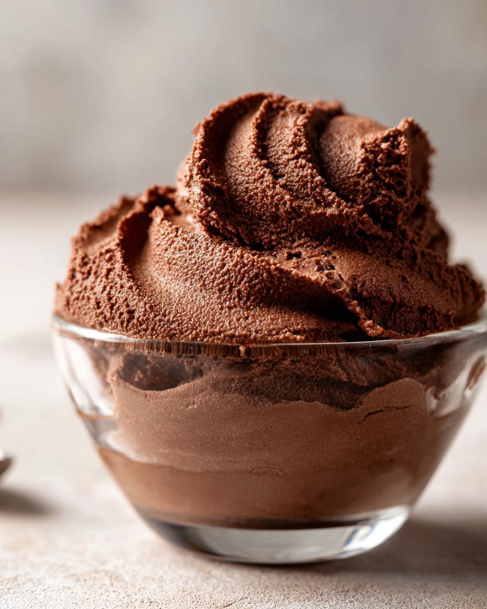 Close-up of rich, dark chocolate mousse piped high in a small clear glass bowl.