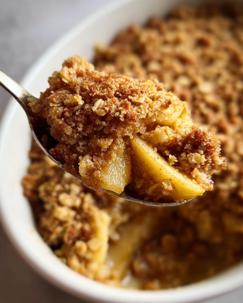 A spoonful of warm apple crumble showing tender cooked apples and a thick, crunchy oat topping.