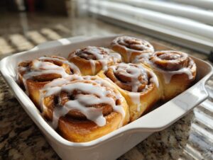 Six freshly baked small batch cinnamon rolls generously drizzled with white icing in a white ceramic dish.