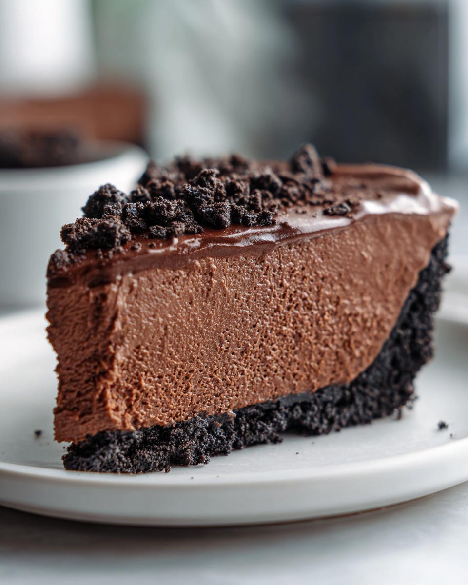 A thick slice of decadent chocolate mousse pie featuring a dark cookie crust and topped with chocolate crumbs.