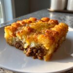 A hearty slice of tater tot casserole featuring a crispy tater tot topping, melted cheese, and a savory ground meat layer.