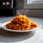 A mound of freshly cooked, steaming Nigerian jollof rice served on a white plate, ready to eat.