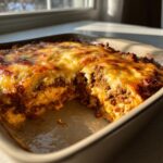 A scoop has been taken out of the hot, cheesy texas trash dip, showing layers of meat and creamy filling.