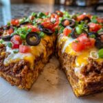 Close-up of a thick slice of Mexican pizza showing layers of seasoned meat, melted cheese, tomatoes, olives, and green onions.