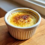 Close-up of a creamy baked egg custard with a caramelized, torched sugar top in a white ramekin.